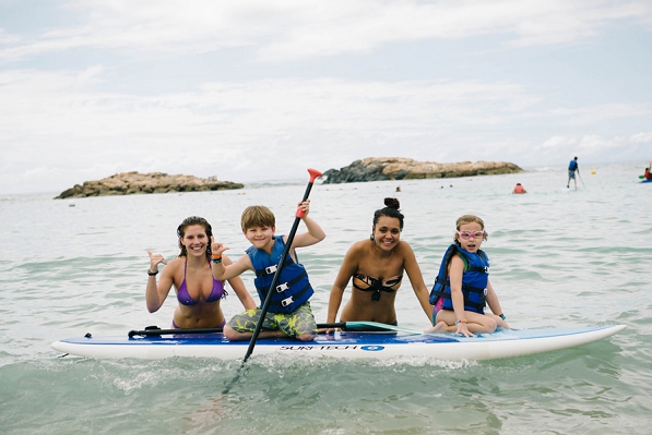 Two kids with their nannies on a paddle board in Ko Olina