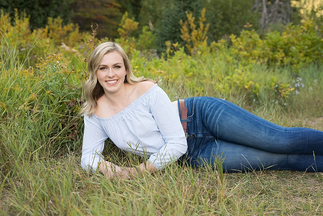 girl in blue off the shoulder shirt laying on her side in summer grasses
