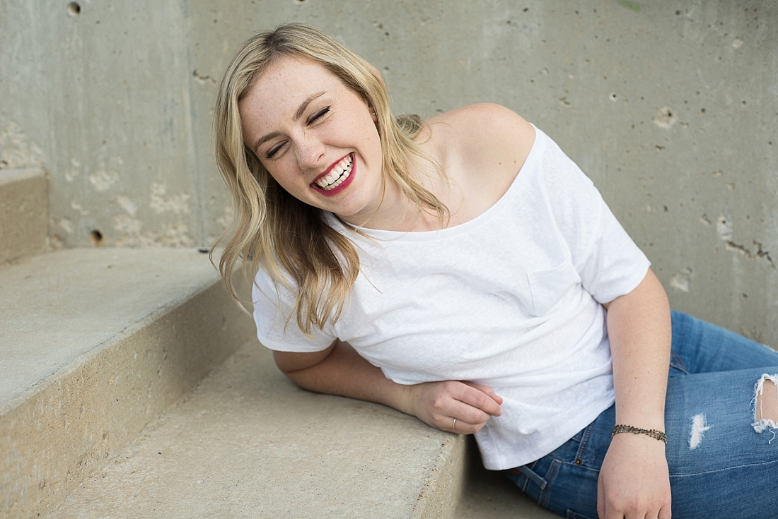 girl sitting on stairs wearing bright red lipstick and a white shirt laughing with her eyes closed