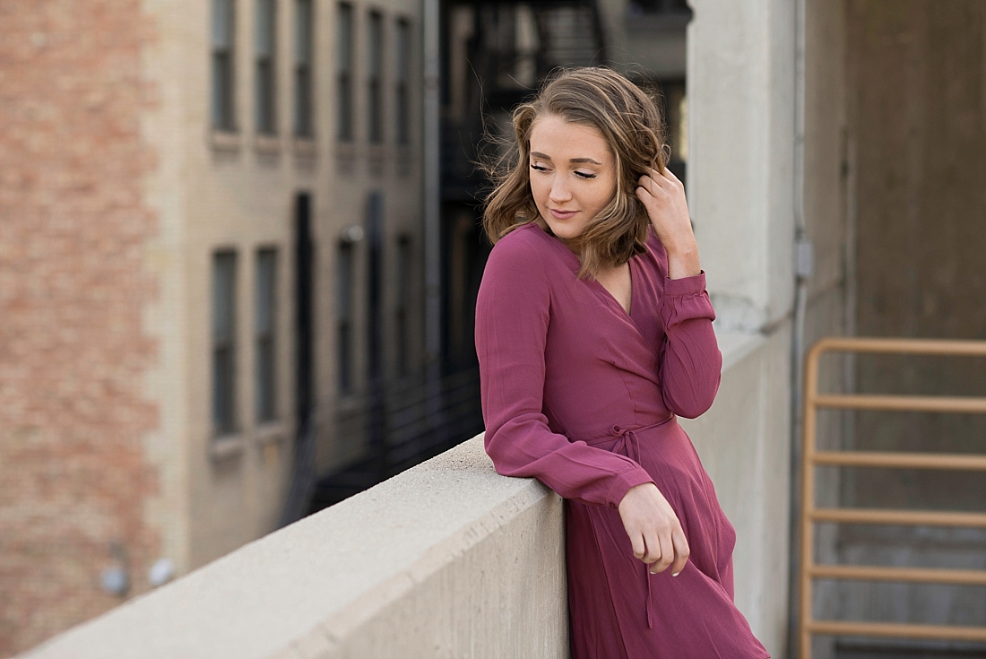 Utah Senior Portraits. Girl on rooftop in maroon dress holding her hair while looking down over her shoulder.