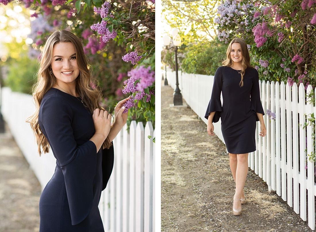 Utah Senior Portraits with girl in navy blue dress by white picket fence lined with purple lilacs