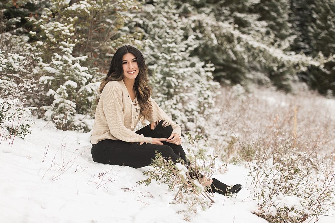 Girl sitting in snow wearing black pants and a tan sweater in cottonwood canyon