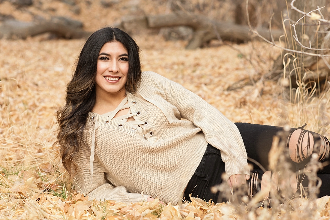 Girl laying in fall leaves with black pants and tan sweater