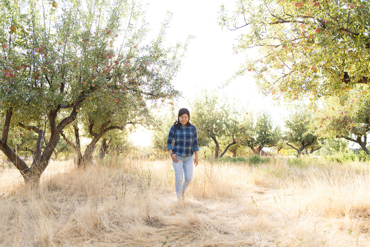 utah senior pictures of girl in blue plaid shirt walking through an apple orchard