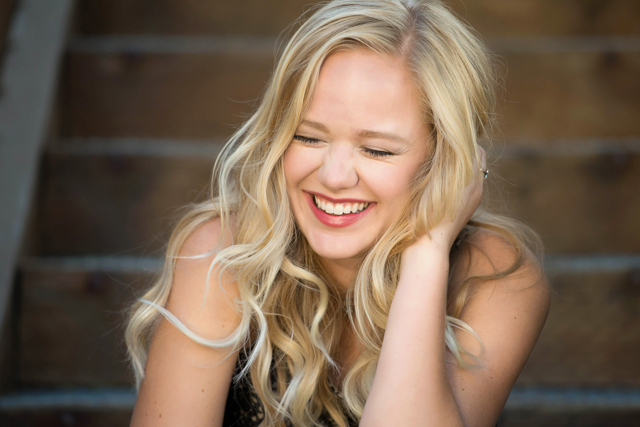 girl with curly blonde hair sitting on stairs laughing