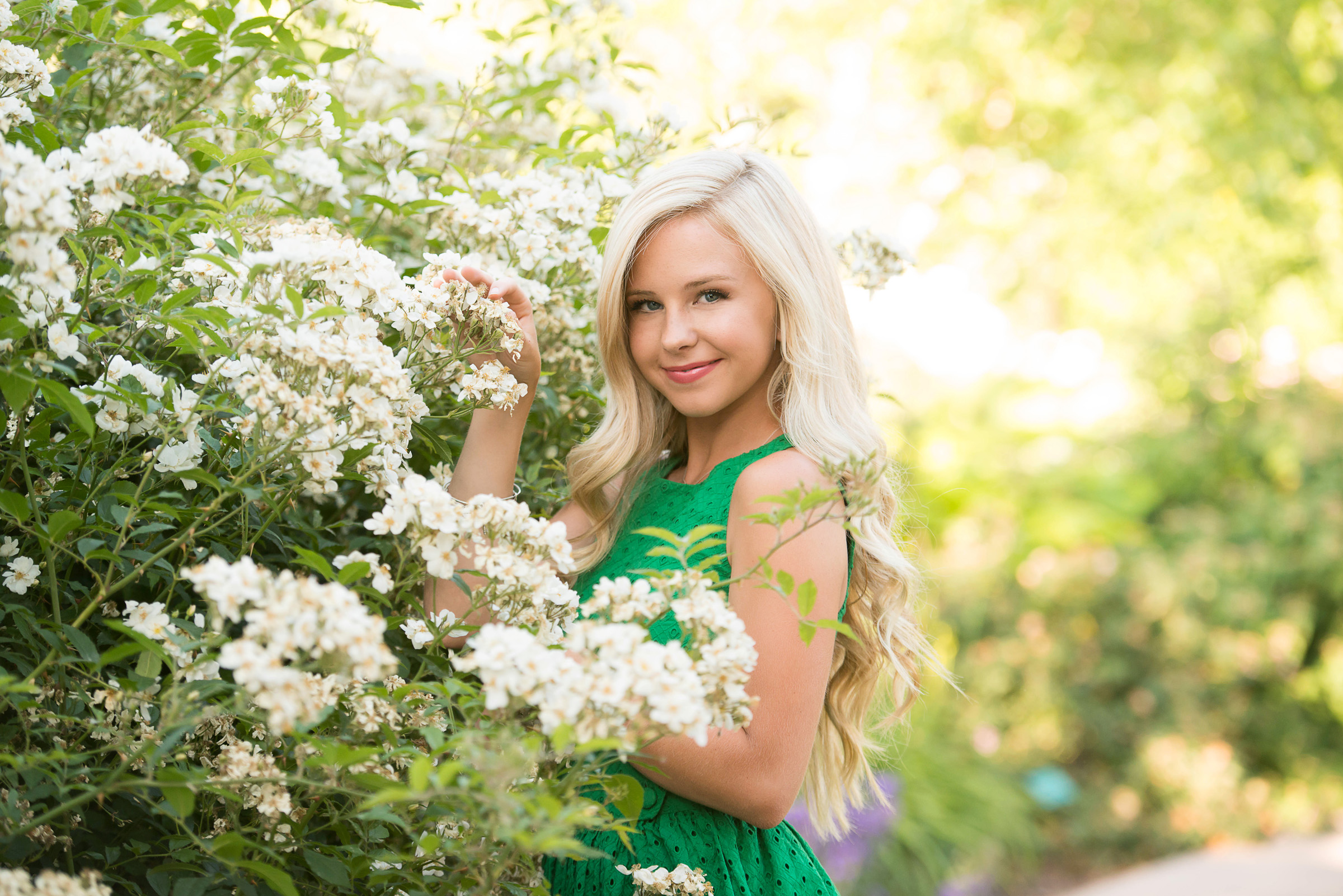 Girl wearing green dress standing by white roses in a garden
