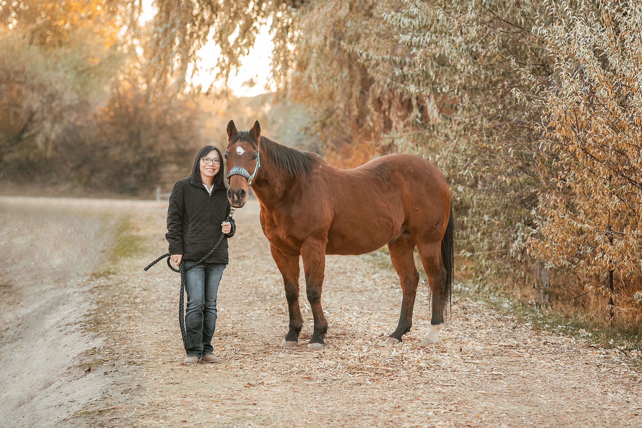 Asian equestrian standing with her horse in the fall leaves