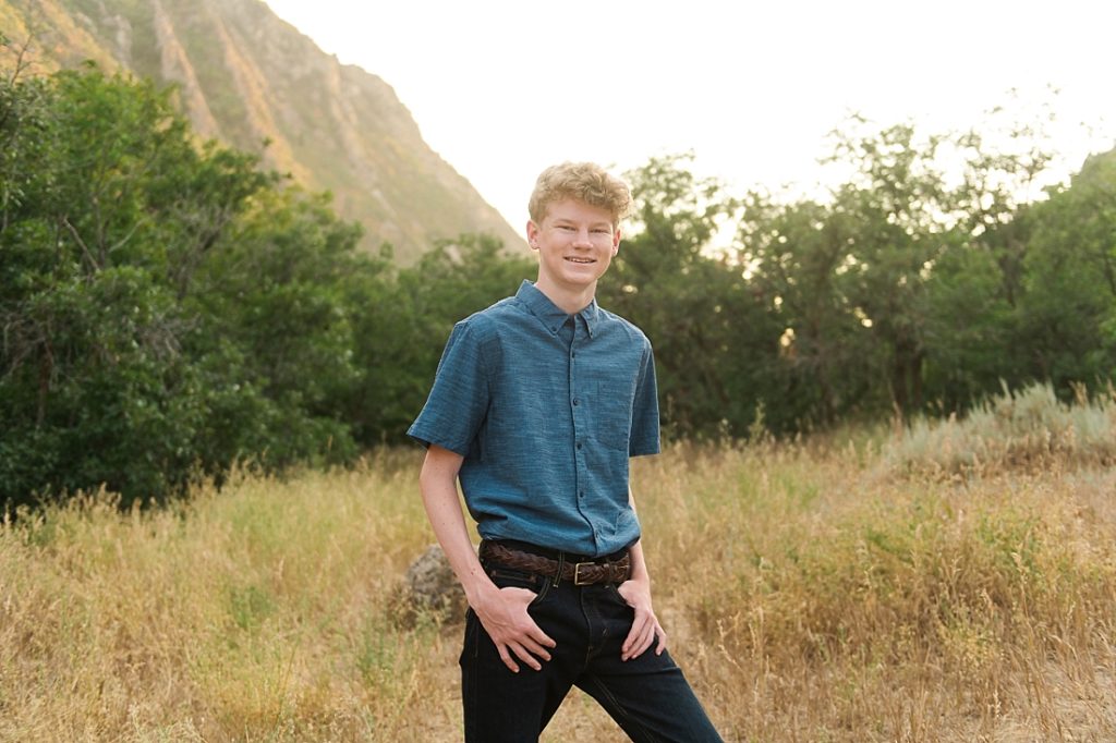 Utah senior portraits with blue button-up shirt standing in a mountain meadow