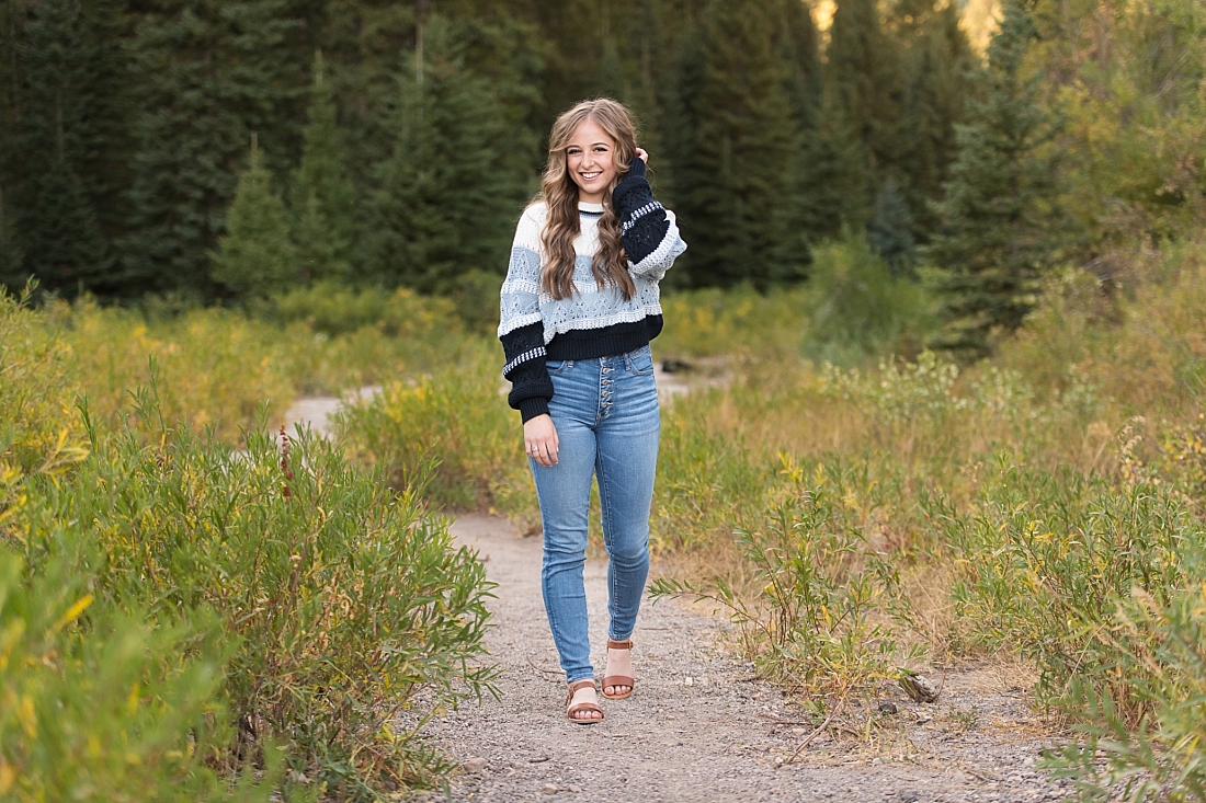 Girl walking down a path in the mountains wearing a blue striped sweater