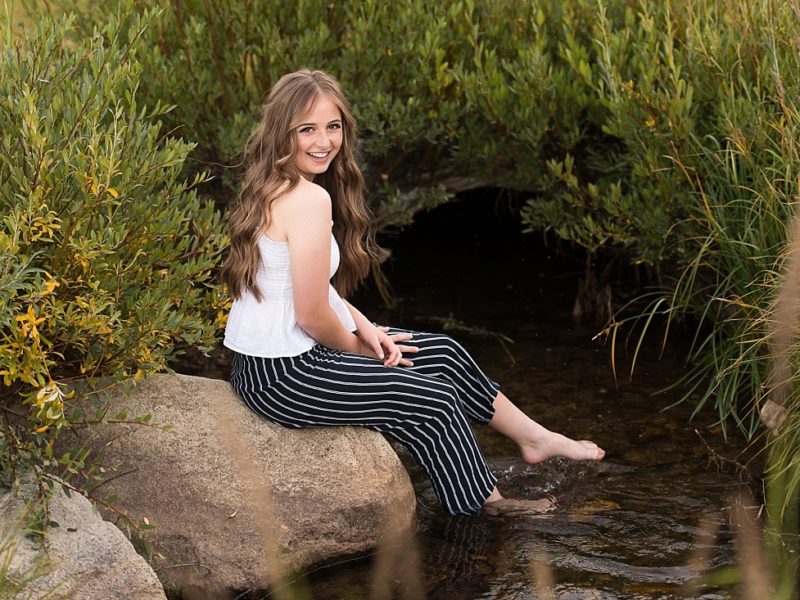 Waterford School senior girl sitting on a rock with her bare feet in the stream