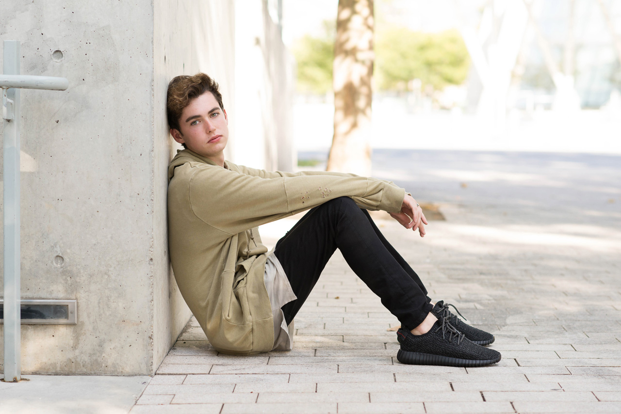 boy sitting against a cement wall wearing hoodie and black pants