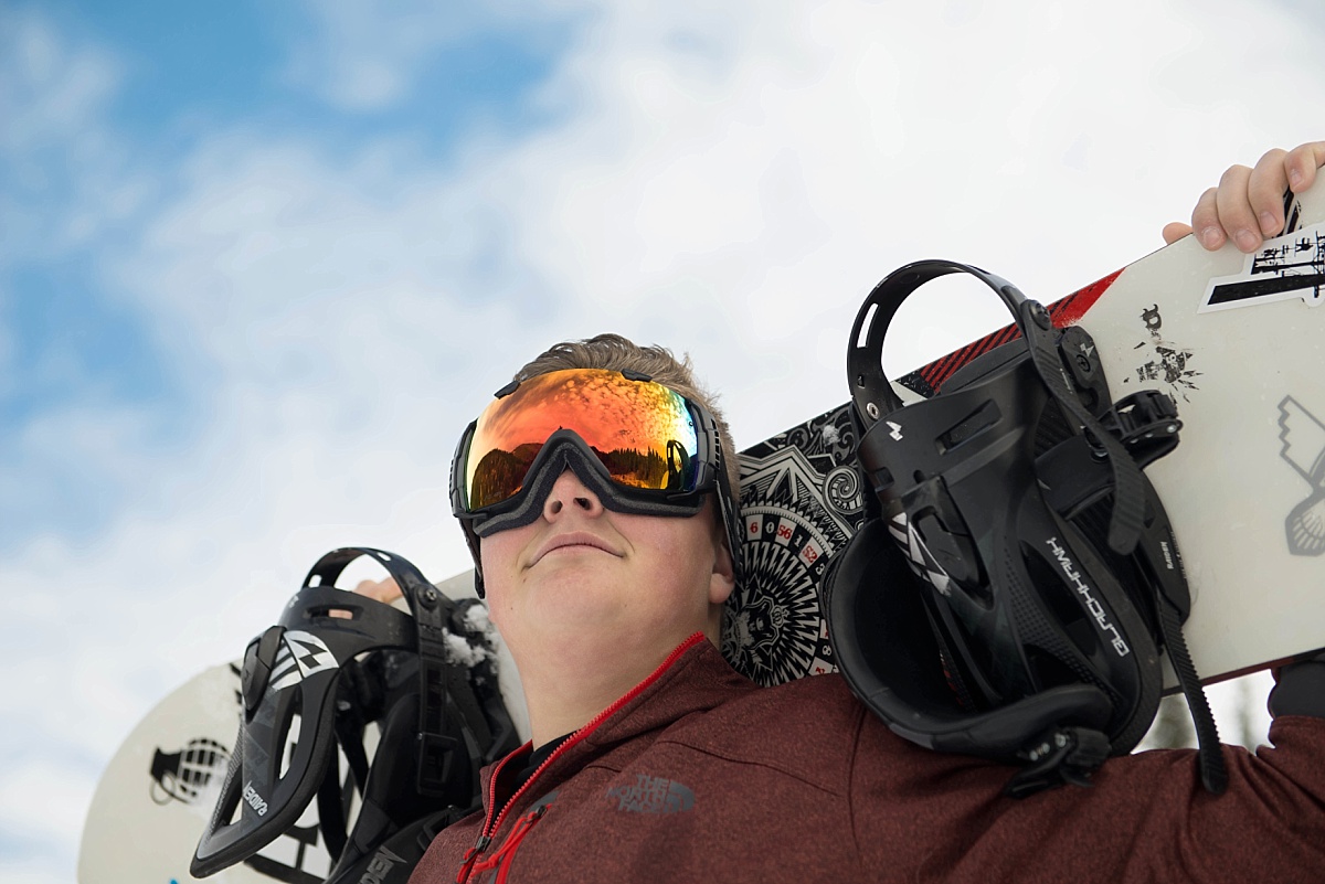 Boy with snowboard behind his neck with his goggles on