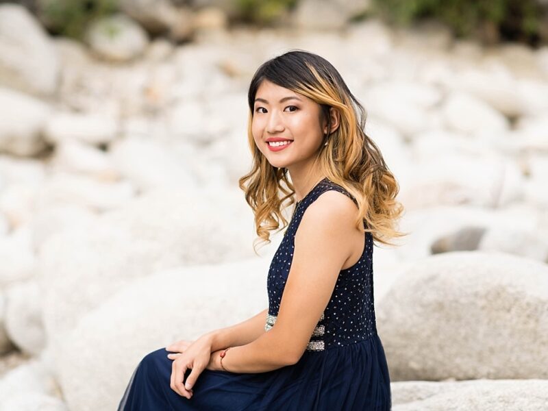 Girl sitting on a rock wearing a navy blue dress with silver spots.