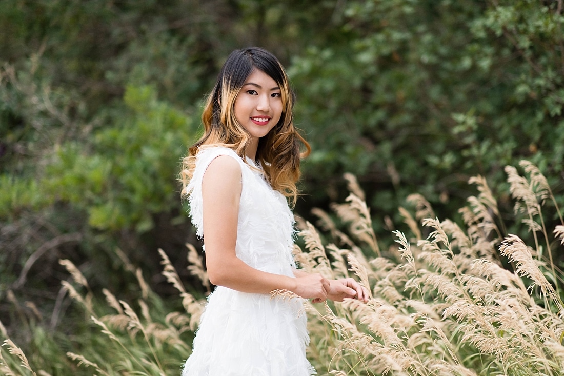 High School Senior Girl in white dress with feathers in tall grass.