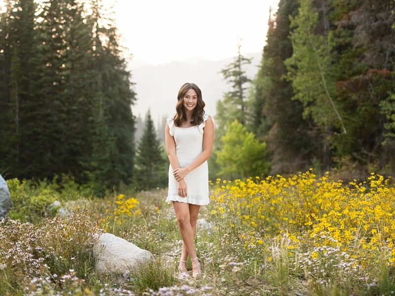 Waterford graduate in white dress standing in wildflowers in the mountains