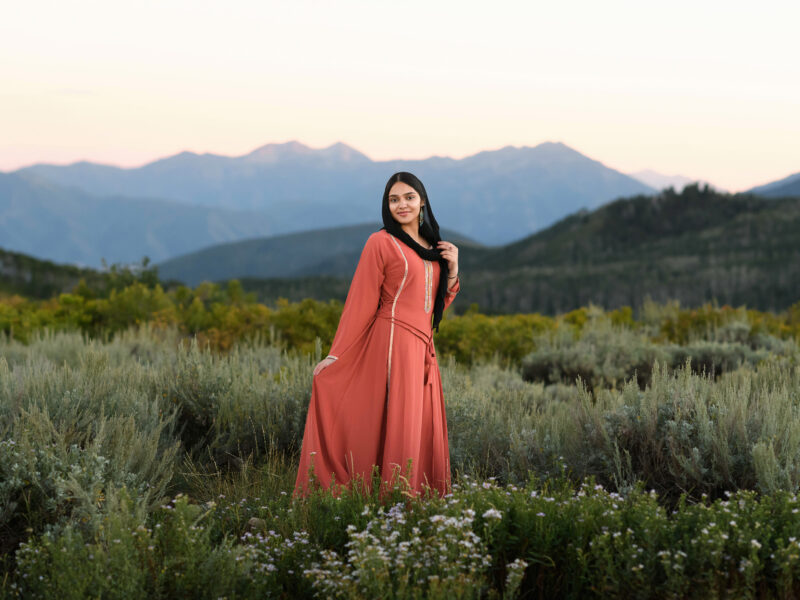 Girl in mountains at sunset wearing a coral dress and black hijab